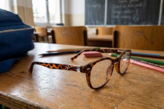Lunettes d'enfant cassées posées sur un bureau d'école en bois avec monture fissurée près de la charnière